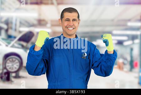 Mature mechanic man wearing yellow gloves and blue uniform standing at workshop excited for success with arms raised celebrating victory smiling. Winn Stock Photo