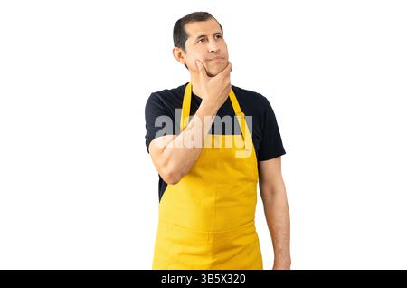 Salesman with yellow apron over isolated white background with hand on chin thinking about question, pensive expression. Smiling with thoughtful face. Stock Photo