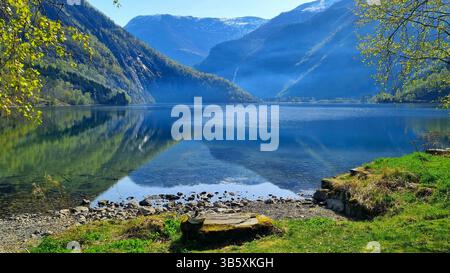 Picturesque landscape with mountains, blue lake Eidsvatnet and beautiful reflections on the water surface on a foggy spring morning in Skjolden, Norwa Stock Photo