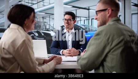 Hispanic Businessman Hands Keys To New Car Owners At Dealership. Stock Photo