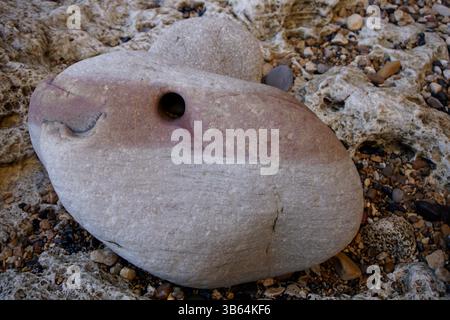 Eroded sedimentary rock with natural hole and colored layers found on a rocky beach.Seaham Beach, England Stock Photo