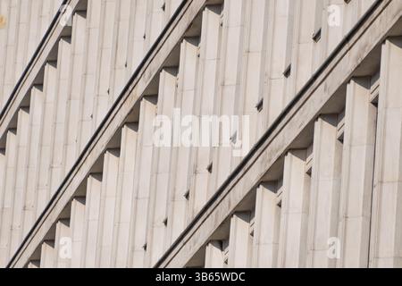 A modernist facade with repeating vertical concrete elements, creating rhythmic patterns and dynamic diagonal shadows. Architecture details. Stock Photo