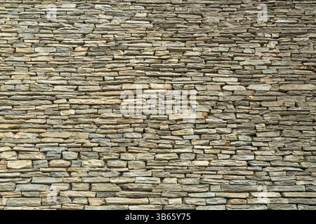 A tightly stacked stone wall with irregular, layered rocks, creating a rustic and textured pattern. Backgrounds Stock Photo