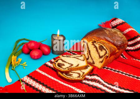 Romanian sweet bread "cozonac", stuffed with walnuts and chocolate, on a red traditional towel, easter eggs and lit candle Stock Photo