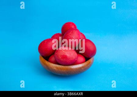 Red boiled easter eggs pile in a wooden bowl on blue background Stock Photo