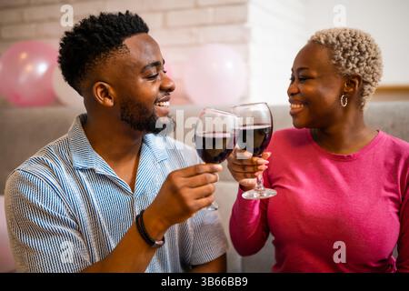 Happy young couple celebrating woman's birthday at home. They are toasting with wine. Stock Photo