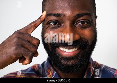 Happy black man is smiling and pointing at his head. Close up portrait of man who is having an idea. Stock Photo