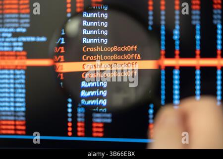 Man's hand uses a magnifying glass to closely examine a computer screen highlighting recurring CrashLoopBackOff error messages, symbolizing the focuse Stock Photo
