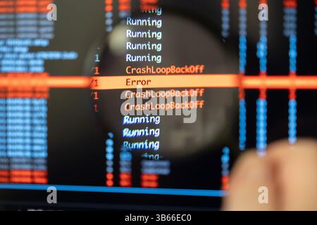A man's hand holds a magnifying glass closely over a screen displaying CrashLoopBackOff and Error messages, symbolizing the intense focus required for Stock Photo