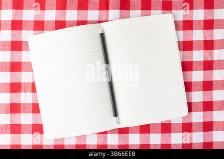 Open blank notebook with a pencil on a red checkered tablecloth surface, perfect for illustrating concepts of writing, recipes, note-taking, planning, Stock Photo