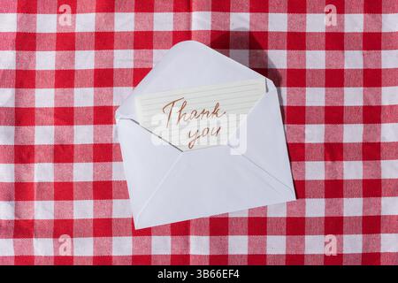 Open white envelope with a Thank you card inside, on a red checkered tablecloth surface, suitable for conveying gratitude and appreciation Stock Photo