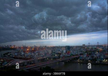 A dramatic thunderstorm approaches Ho Chi Minh City, Vietnam, with heavy storm clouds over the skyline and Saigon River at twilight. Stock Photo