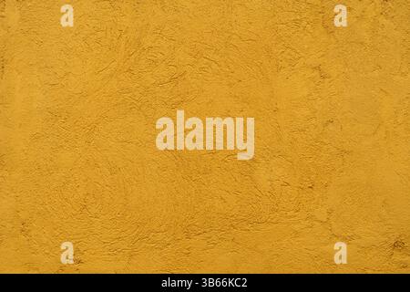 Yellow painted wall with rustic stucco texture. The finish shows organic patterns and a grainy surface ideal as a decorative background. Stock Photo