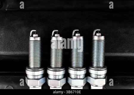 Car Spark Plugs, Close-up of four new iridium spark plugs are lined up against a dark background. DIY engine repair Stock Photo