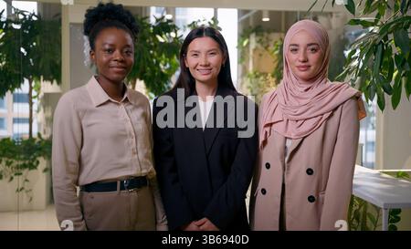 Three beautiful multiracial girls ethnic diversity business women students friends coworkers businesswomen smiling looking at camera African Muslim Stock Photo