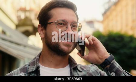 Smiling guy Caucasian man businessman male tourist cheerful joyful happy talking mobile phone on street outdoors casual conversation smartphone call Stock Photo