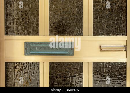 Close-up of a scratched golden metal door with textured glass, an Italian mail slot labeled "Lettere", a metallic handle and a lock. Vintage European Stock Photo