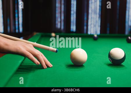 Hand holding a cue stick and aiming a billiard ball on a green felt pool table, indoor bar game sports Stock Photo