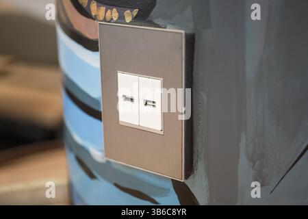 A public cell phone charging device on a wall, featuring two electrical sockets for cables. Stock Photo