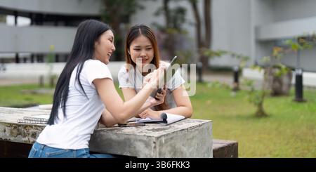 Study Group and Collaboration. Two students enthusiastically discussing their assignments on a tablet in a campus park. Stock Photo