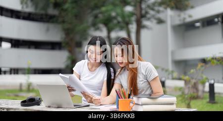 Creativity and Study Sessions. Two young friends immersed in homework, utilizing technology and collaboration skills at their study spot. Stock Photo