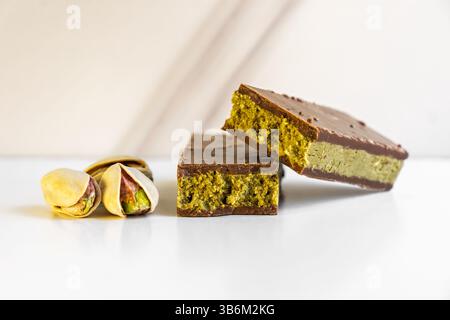 Chocolate bars with pistachio cream filling lying on white reflective surface with pistachios Stock Photo