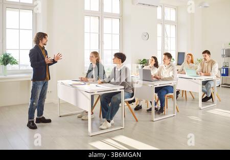 Male teacher conducting lesson in classroom while university students listening and taking notes. Stock Photo