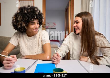 Two female university students collaborating on a project at home, sharing ideas and smiling Stock Photo