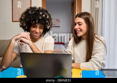 Two happy female students collaborating on laptop at home Stock Photo