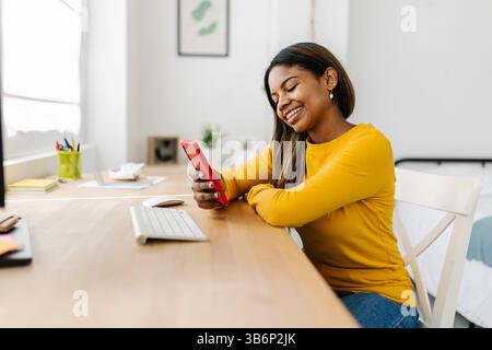 Smiling freelancer using smart phone at home office desk Stock Photo
