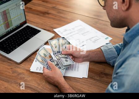 Mature male counts cash money over utility bills at laptop in business office financial work Stock Photo