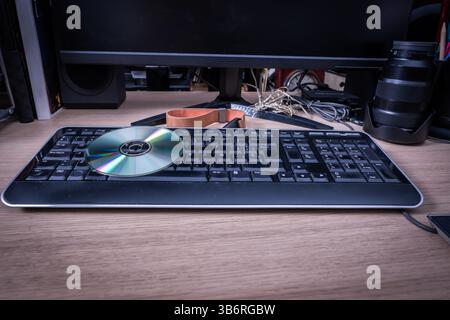 Compact disc laying on a computer keyboard, suggesting data transfer or software installation in a retro tech environment Stock Photo