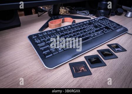 Retro computer keyboard and photo slides laying on wooden desk with monitor in background, showing transition from analog to digital photography Stock Photo