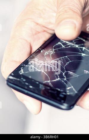 A hand grips a smartphone showing a shattered screen, indicating an accident or mishap. The background features elements of city life, emphasizing the Stock Photo