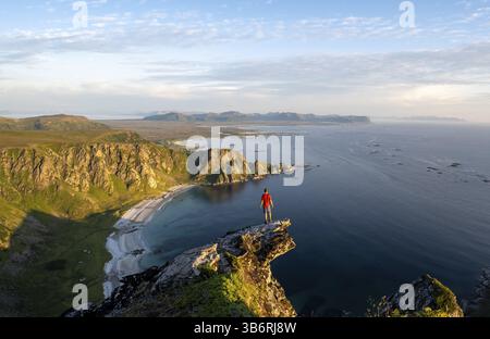 Evening mood, mountaineer standing on a rocky outcrop on the summit of Matind, view of coastal landscape, Hoyvika beach and sea, Matinden, Andoya Stock Photo