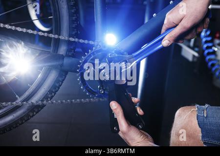 A close-up of a male bicycle mechanic's hand in the workshop uses a screwdriver tool to adjust and repair the bicycle crank assembly, the front bike s Stock Photo