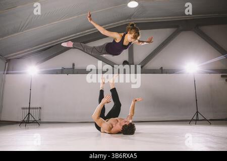 Young couple Couple practicing acro yoga in gym. Healthy lifestyle. Acroyoga. Couple yoga. Partner yoga. Muscular man throwing women to air. Concept o Stock Photo