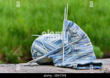 light-blue sock yarn in the process of knitting socks, with knitting needles, lying on a stone surface Stock Photo