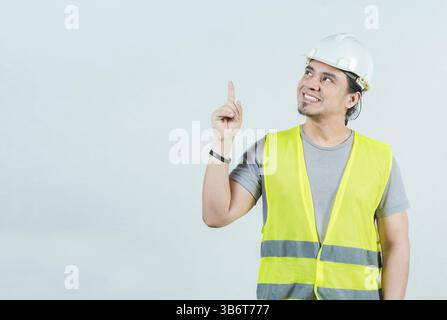 Smiling engineer pointing up isolated. Happy young builder with helmet pointing up Stock Photo