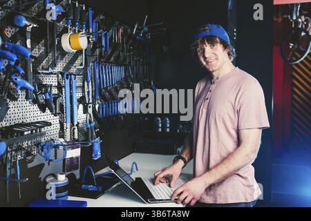 Theme business profession manager and technology. Young stylish Caucasian male owner bicycle shop uses a laptop computer near the stand with the tools Stock Photo