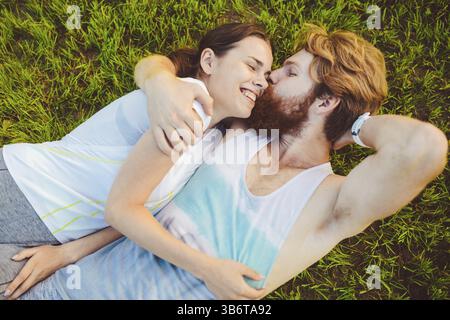Theme is sport and a healthy lifestyle. A young man and woman couple are resting on their backs on the green grass, a lawn in a pack after playing spo Stock Photo