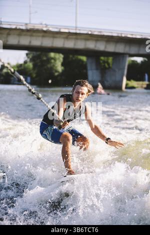 Active wakesurfer jumping on wake board down the river waves. Surfer on wave. Male athlete training on wakesurf training. Active water sports in open Stock Photo