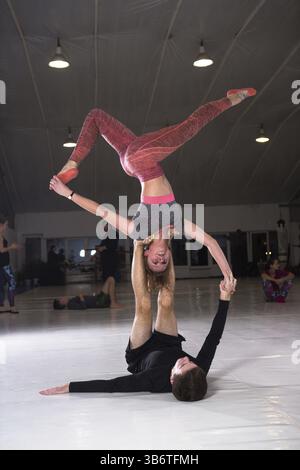 Young couple practicing acroyoga on a mat in the gym together. Woman flies. Man and woman sport training acrobatics yoga inside. Affiliate yoga, flexi Stock Photo