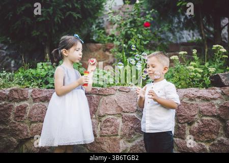 Two children in the park blowing soap bubbles and having fun. Two baby Playing With Soap Bubbles. brother and sister having fun outdoors, happy childh Stock Photo
