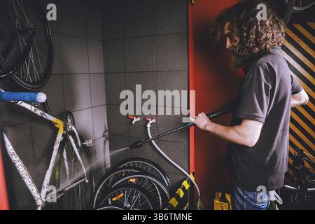 Services professional washing of a bicycle in the workshop. Close-up of hand Young Caucasian stylish man doing bicycle cleaning using automatic electr Stock Photo