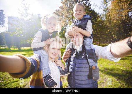 Lovely young couple taking selfie photo self portrait carrying son and daughter on shoulders posing happy smile. Point View Shot Father, mother Childr Stock Photo