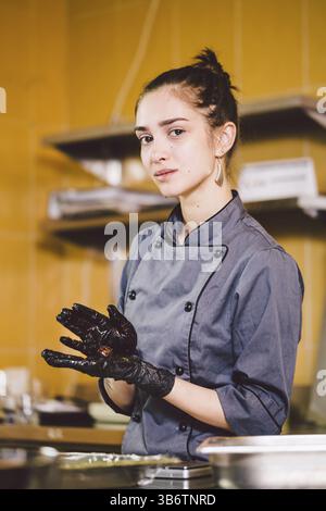 Subject profession and cooking pastry. young Caucasian woman with tattoo of pastry chef in kitchen of restaurant preparing round chocolate candies han Stock Photo