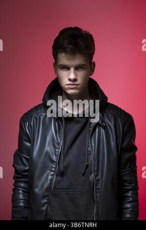 Cute brutal man in black leather jacket model style. portrait of a handsome guy on pink studio background. Man In Black Jacket. Young Fashion Man In L Stock Photo