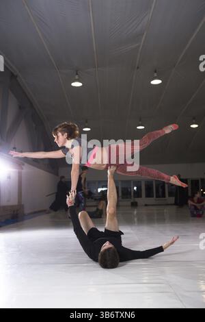 Young couple practicing acroyoga on a mat in the gym together. Woman flies. Man and woman sport training acrobatics yoga inside. Affiliate yoga, flexi Stock Photo
