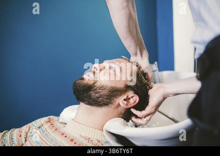 Barbershop theme. Hairdresser for washing hair in a barbershop. Hands male hairdresser close-up washes hair with foam and shampoo Caucasian man with b Stock Photo